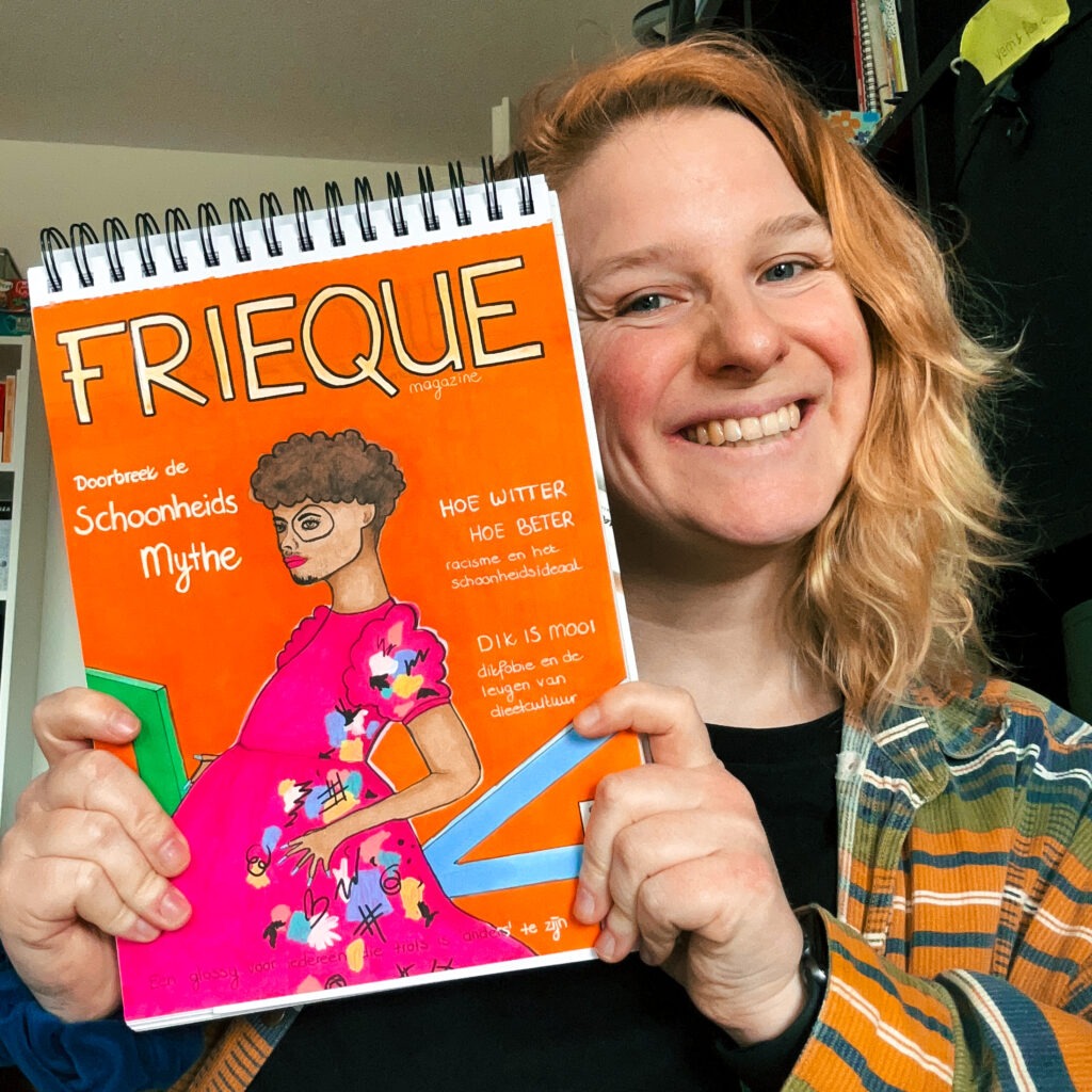 Wendy kijkt lachend naar de camera met de getekende eerste versie van de cover van FRIEQUE in haar handen. De cover is oranje met geometrische, gekleurde vormen op de achtergrond. Op de voorgrond is een model te zien met donker krullend haar, een getinte huid, een baard en snor, makeup en een roze jurk met vlekken en strepen in verschillende kleuren.