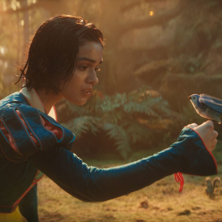 Scene uit de film Snow White. Rachel Zegler als Sneeuwwitje houdt een vogel op haar hand en kijkt ernaar. Op de achtergrond zijn eekhoorns en bomen te zien.